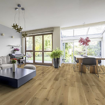 Ambiente Bild, großes helles Wohnzimmer mit beiger Couch und langem Esstisch, Im Hintergrund ist eine große Fensterwand, Hauptbestandteil des Bildes ist der Naturparkettboden aus Eichendielen