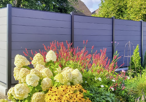 Gartenbild, im Vordergrund sind bunte Blumen und dahinter dunkelgrau WPC Sichtschutzzäune