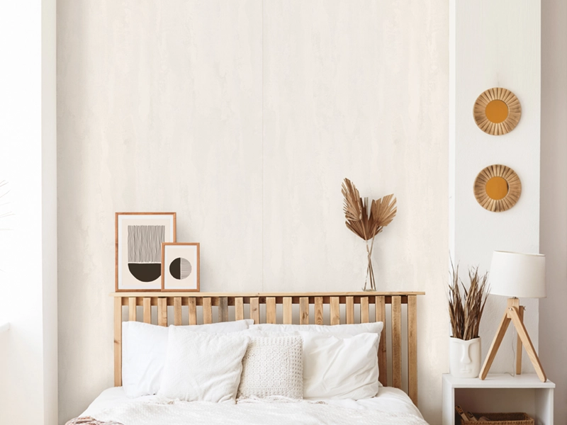 Helle SPC Platten an Schlafzimmerwand. Davor getrocknete goldene Palmblätter in einer Glasvase und zwei Fotorahmen auf dem Kopfteil des Bettes. Stilvolle, trendige Dekoration.