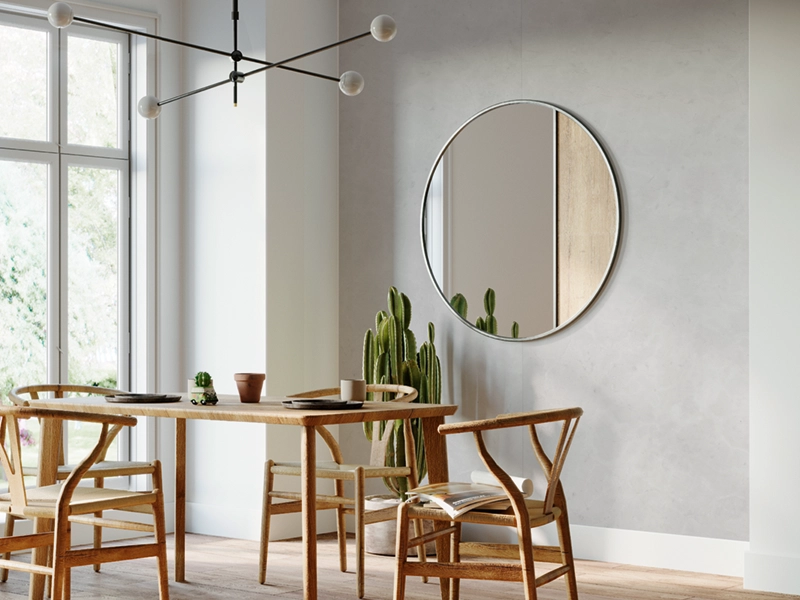 Cleanes, modernes und sehr helles Esszimmer mit Holzesstisch und vier Holzstühlen. Großer, runder Spiegel an Wand, die mit grauen SPC Platten versehen wurde.